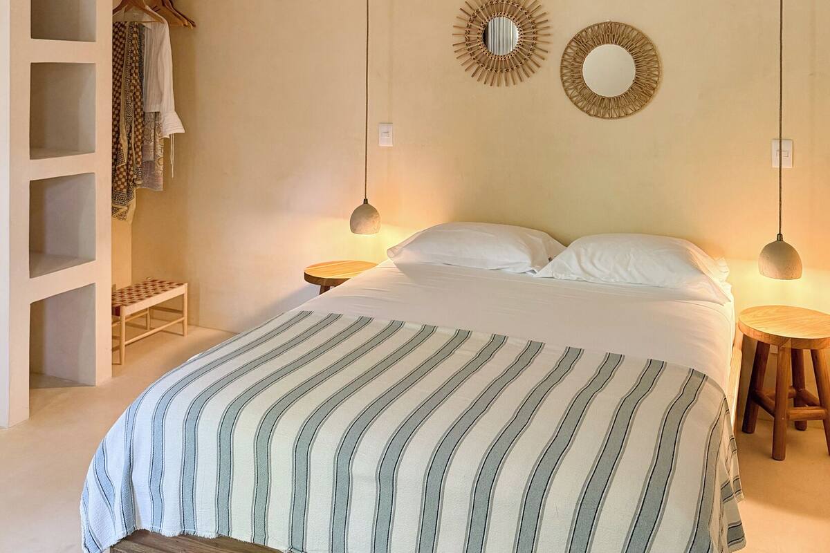 Ein Schlafzimmer mit einem Bett, einem Deckenventilator, zwei Wandleuchten, einem Kleiderschrank und einer Bank.