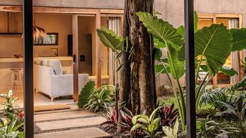 A modern interior with a white sofa, a wooden dining table, and a large tree surrounded by various plants.