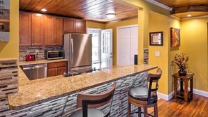 A kitchen with granite countertops, wooden cabinets, a stainless steel refrigerator, and a built-in microwave. - Lovely Cottage w/ Sauna & Fire Pit Near Asheville! (Swannanoa)
