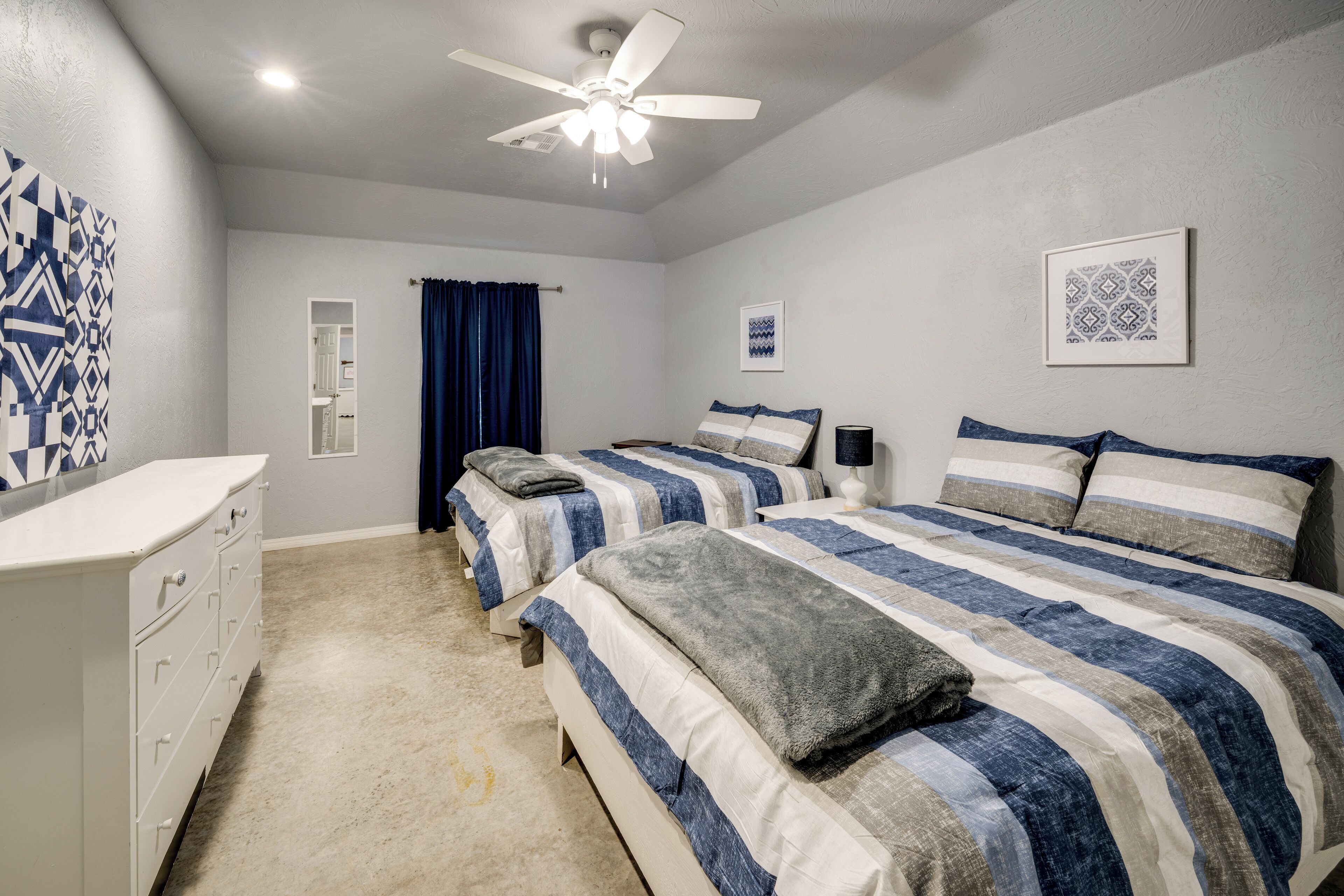 A bedroom with two beds, a ceiling fan, and a dresser.