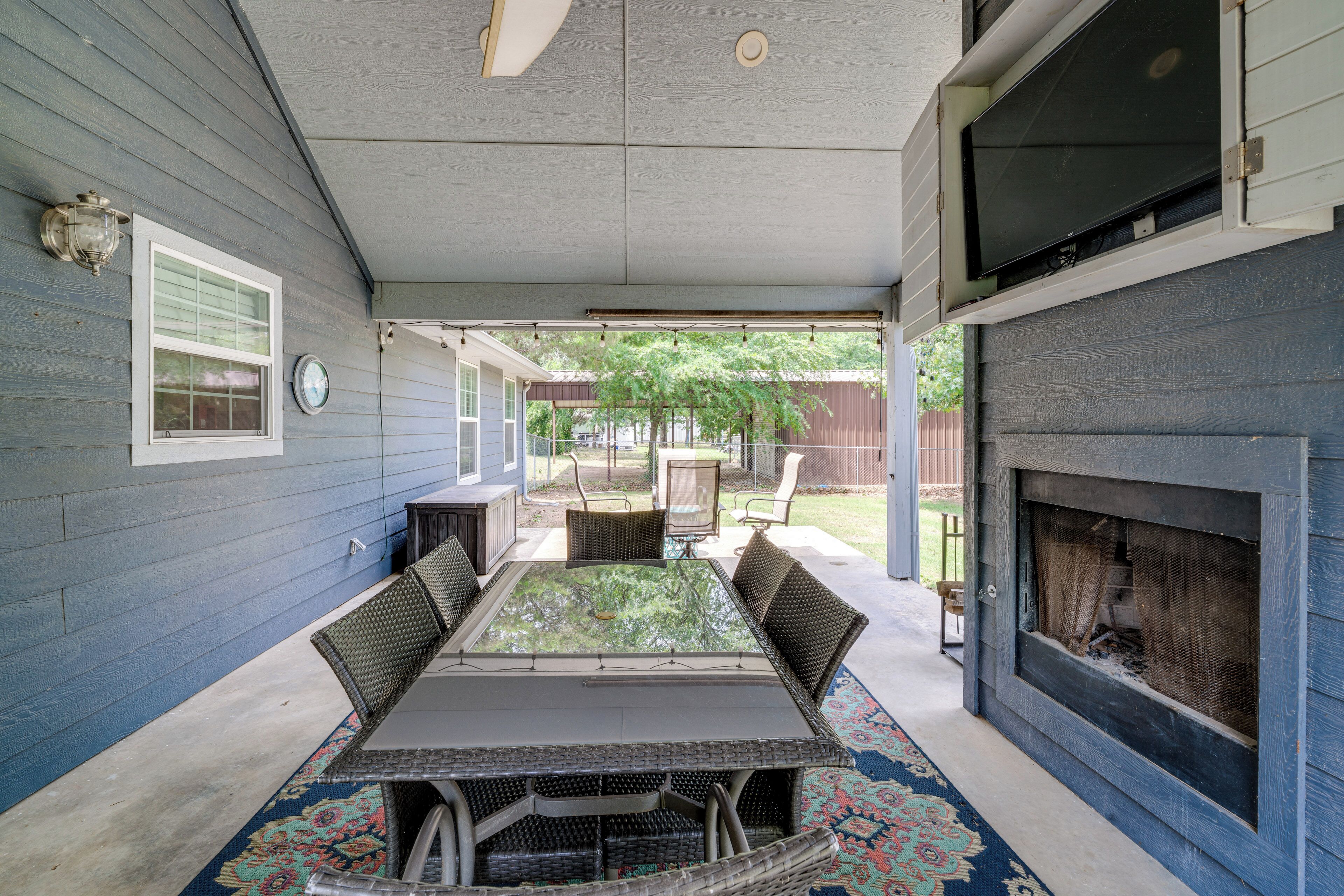 A covered patio with a glass-top table and chairs, a fireplace, and a view of the backyard.
