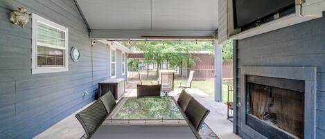 A covered patio with a glass-top table and chairs, a fireplace, and a view of the backyard.
