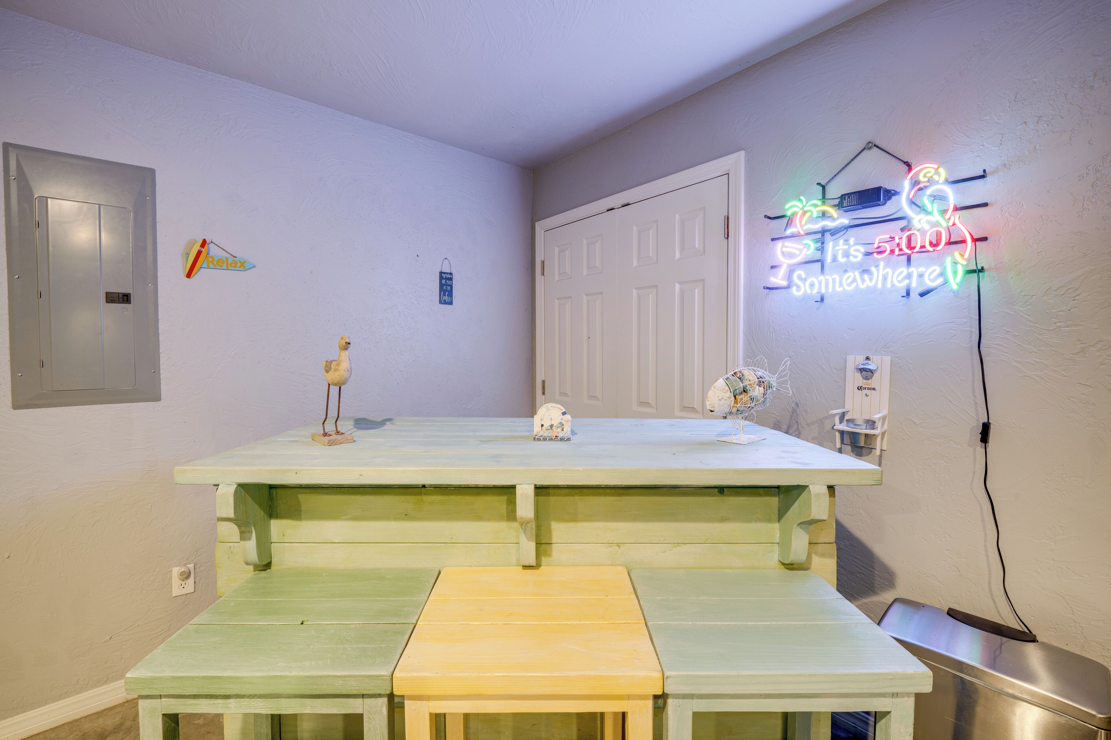 Une pièce avec une table et un banc verts, une porte blanche et un panneau lumineux au néon sur le mur.