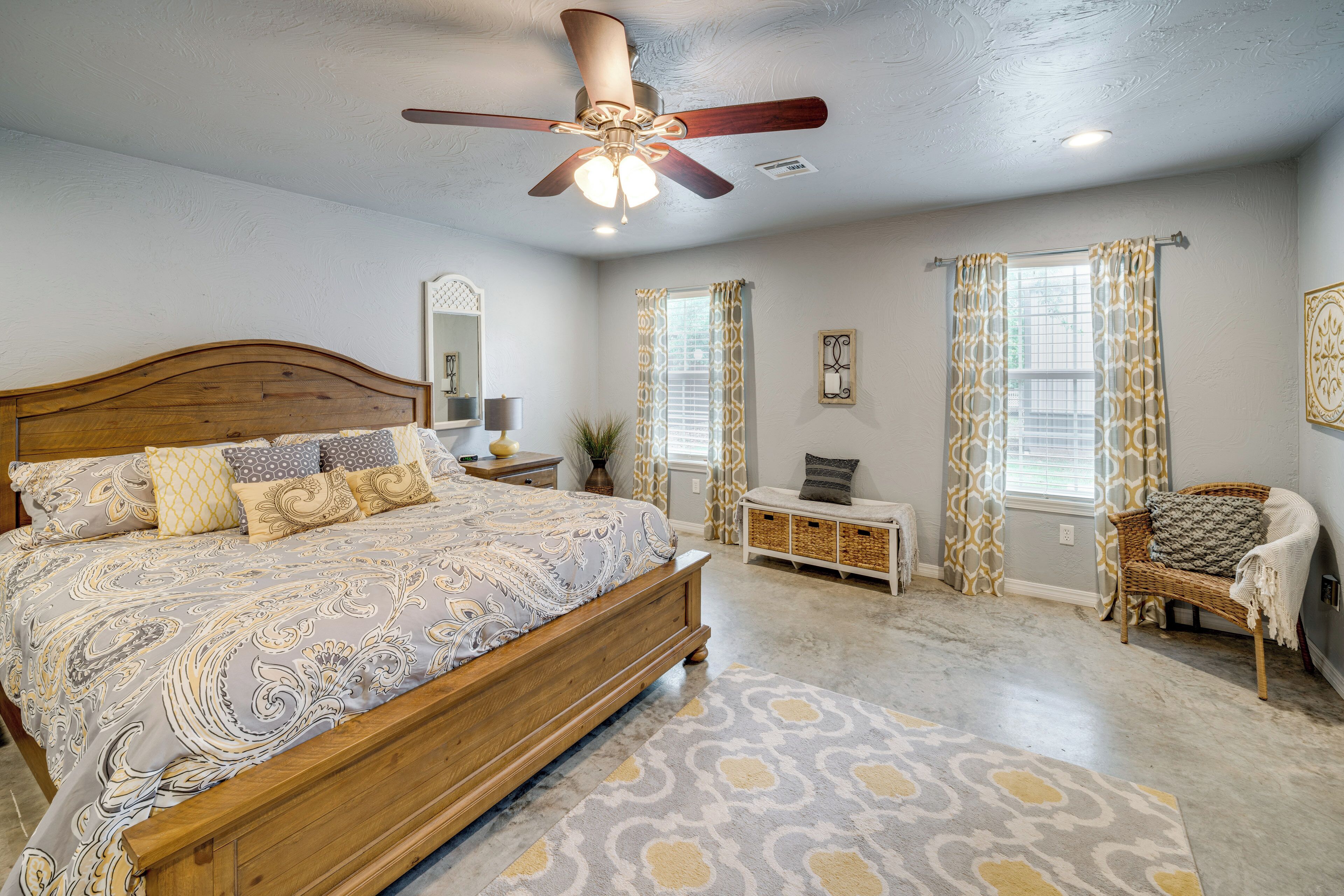 A bedroom with a wooden bed, a ceiling fan, a nightstand, a chair, and a window with curtains.