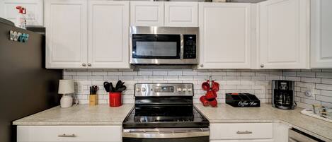 A modern kitchen with white cabinets, stainless steel appliances, and a coffee maker.