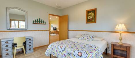 A bedroom with a bed, a desk with drawers, a chair, a bedside table with a lamp, and a mirror on the wall.