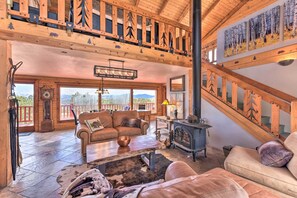 A spacious living area with a high ceiling, wooden beams, a fireplace, and a large window overlooking a mountainous landscape. - Secluded Cotopaxi Cabin w/ Panoramic Mtn Views (Cotopaxi)