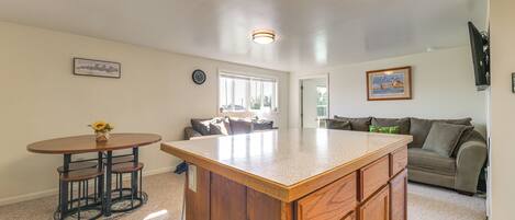 A kitchen with a wooden island, a dining table with stools, a sofa, and a TV mounted on the wall.