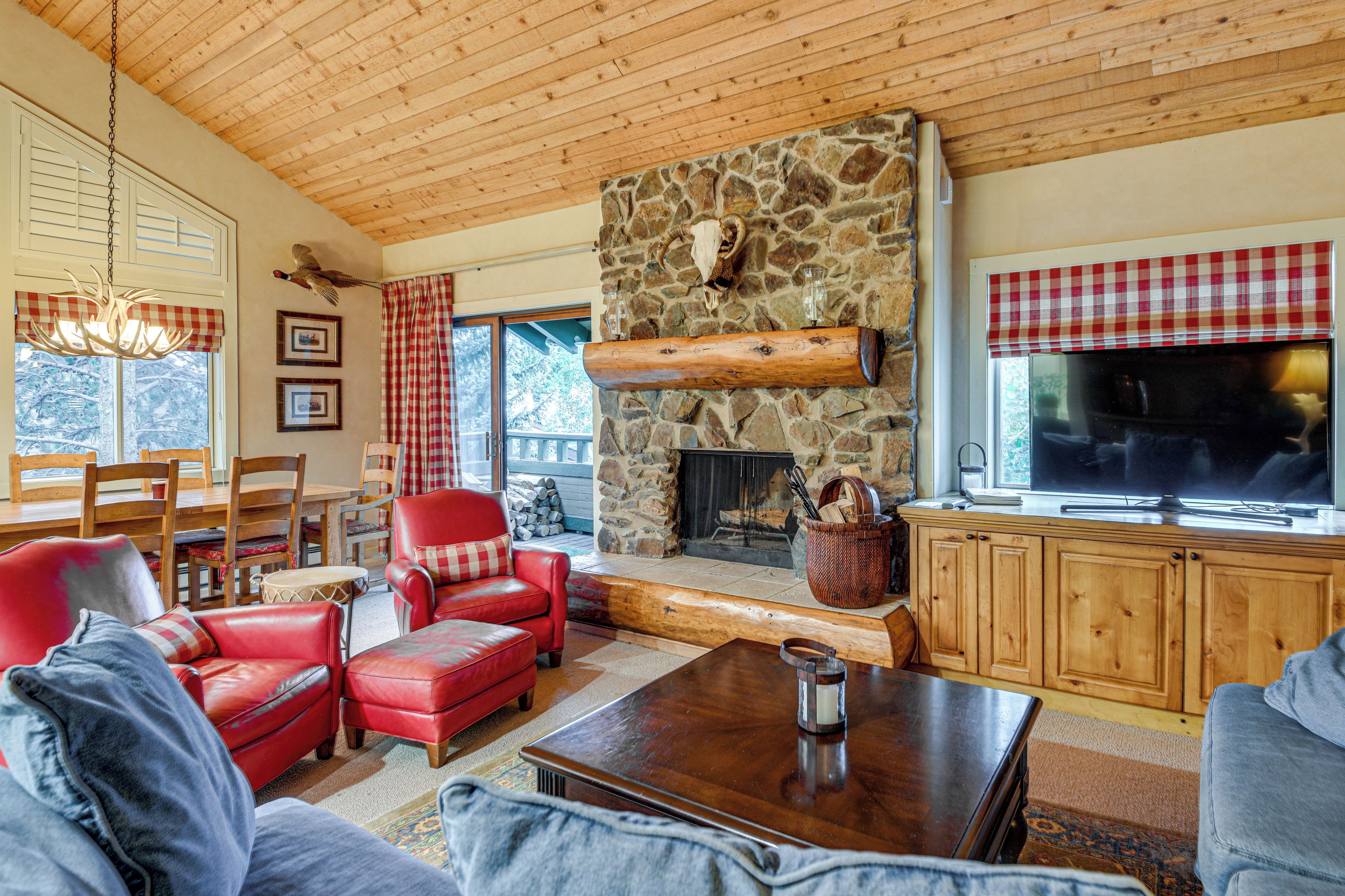 A cozy living room with a stone fireplace, wooden ceiling, and a television.