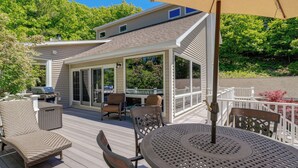 Une terrasse extérieure couverte, aménagée avec des meubles en osier, un barbecue et une table avec un parasol.