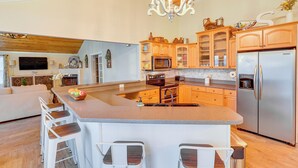 A spacious kitchen with a central island, wooden cabinets, stainless steel appliances, and a chandelier. - Lake Sinclair: Since Day 1 Family Lake House (Milledgeville)