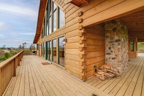 Una cabaña de madera con terraza, ventanas amplias y un muro de piedra.