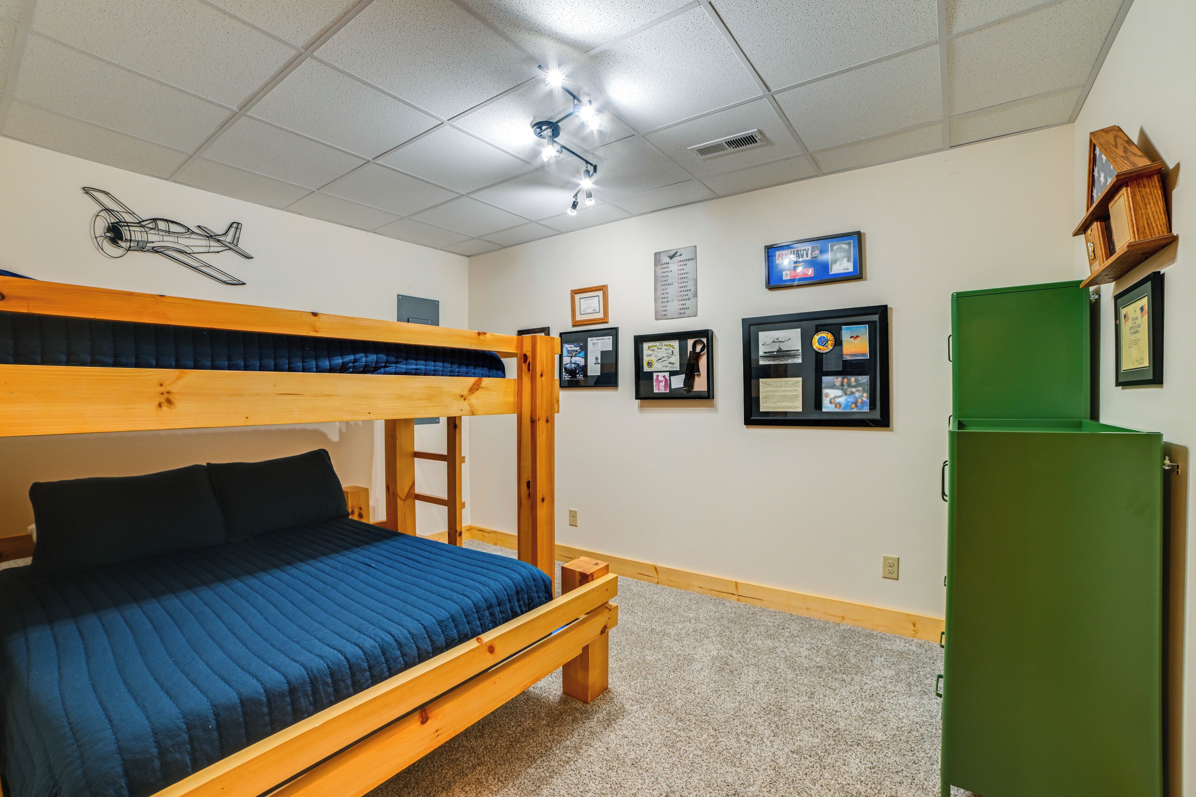 A bunk bed room with a blue mattress, a green cabinet, and framed pictures on the wall.