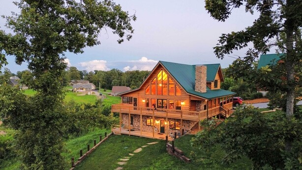 A large, multi-story log cabin with a prominent chimney, a balcony, and a stone foundation. - Large Deck & Shared Dock: Cabin on Kentucky Lake! (Gilbertsville)