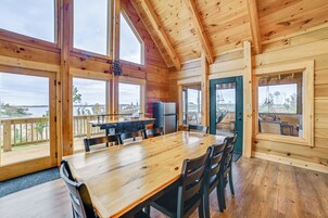 Una cabaña de madera con comedor, ventanas amplias y vistas al exterior.