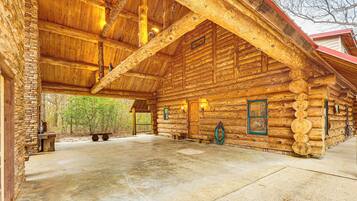 A log cabin with a stone exterior, a large open porch, and a concrete floor.