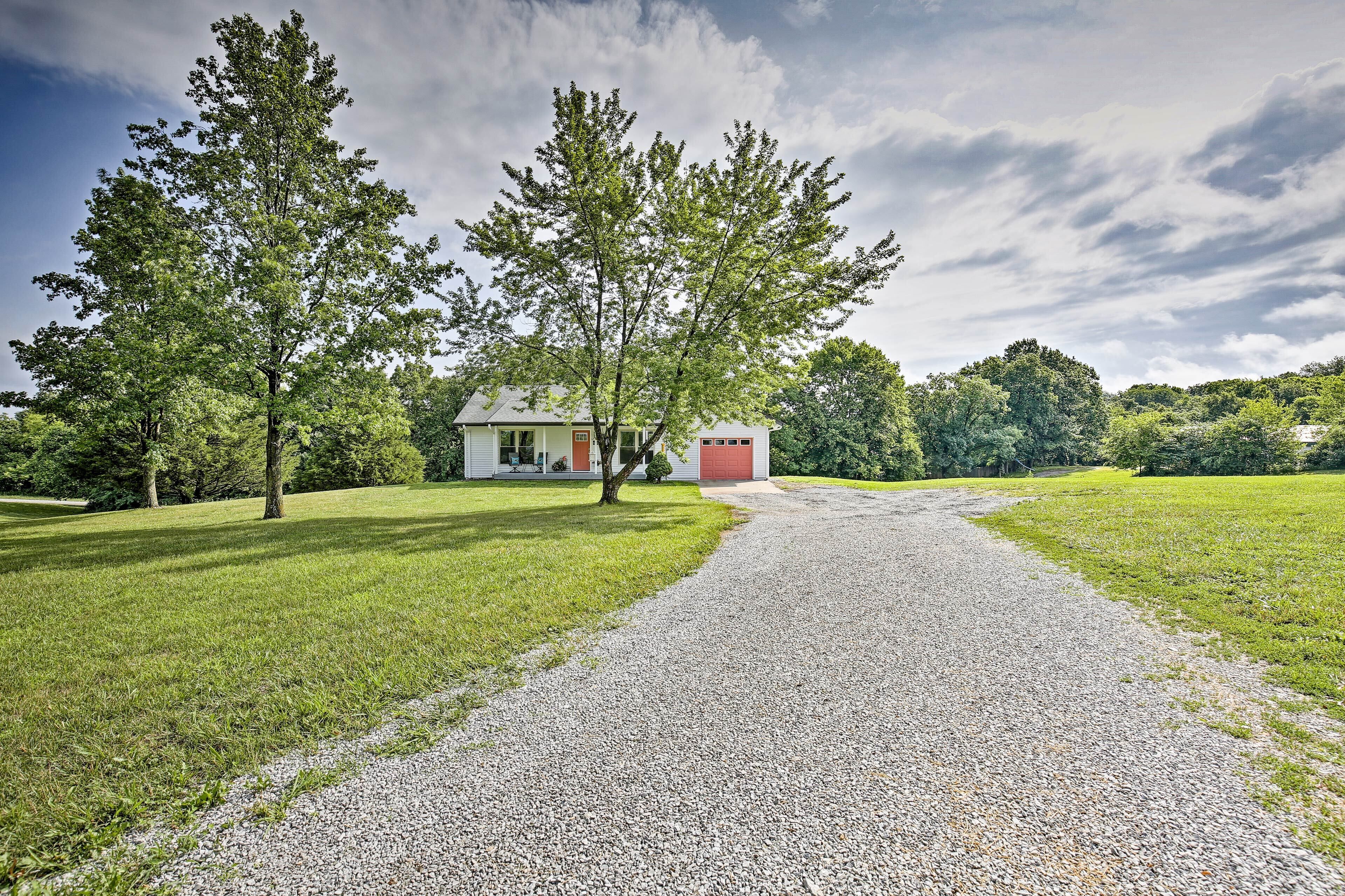A gravel path leading to a house with a red door, surrounded by green grass and trees.