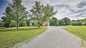 A gravel path leading to a house with a red door, surrounded by green grass and trees.