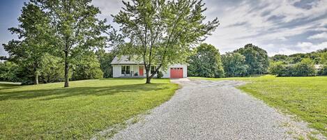 A gravel path leading to a house with a red door, surrounded by green grass and trees.