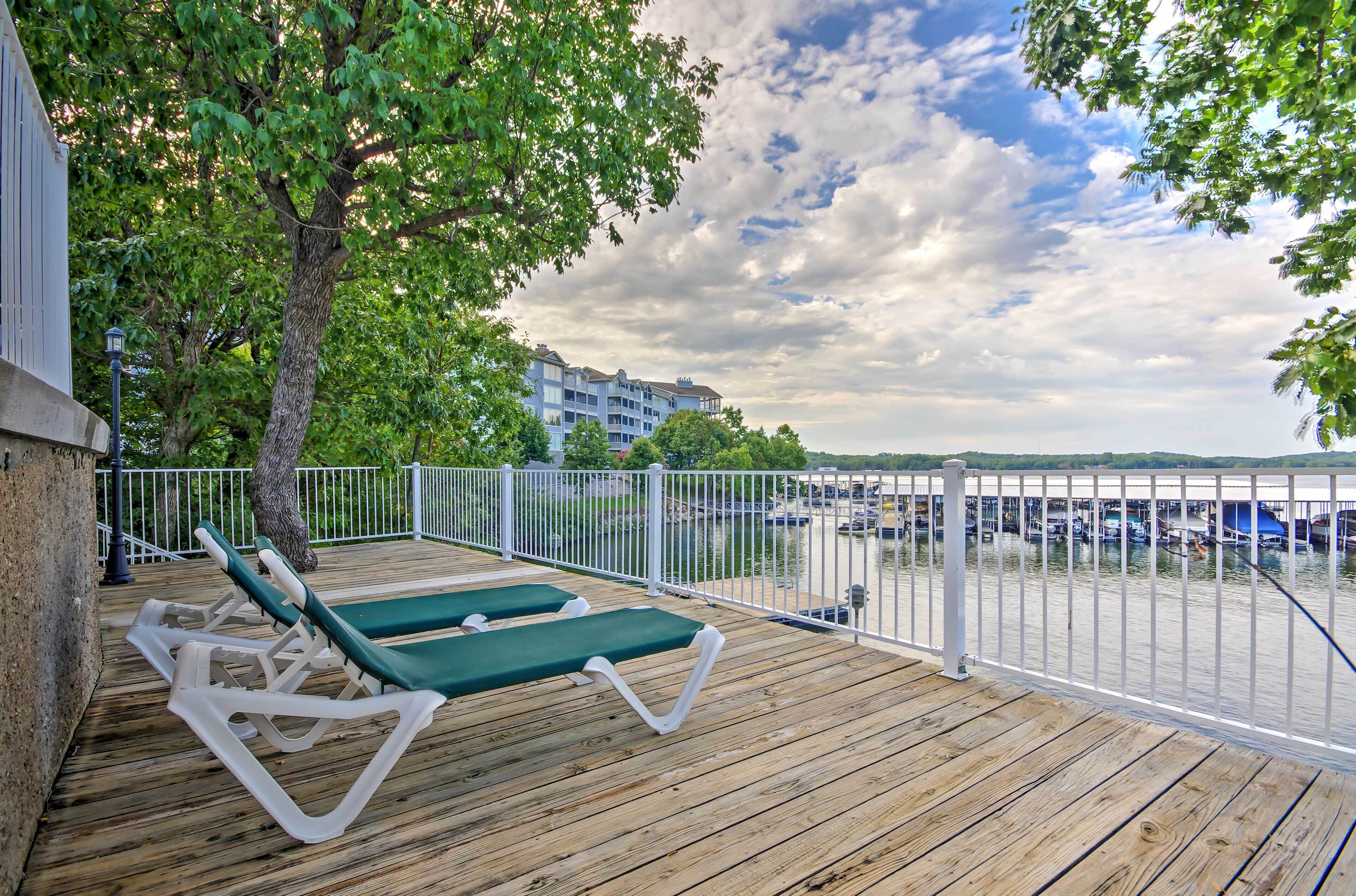 Eine Holzterrasse mit Liegestühlen, ein weißer Zaun und Blick auf einen Jachthafen mit Booten.