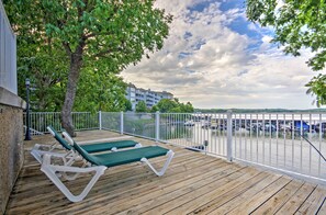 A wooden deck with lounge chairs, a white fence, and a view of a marina with boats. - Luxe Lakeside Regatta Bay Getaway w/ Pool Access! (Lake Ozark)