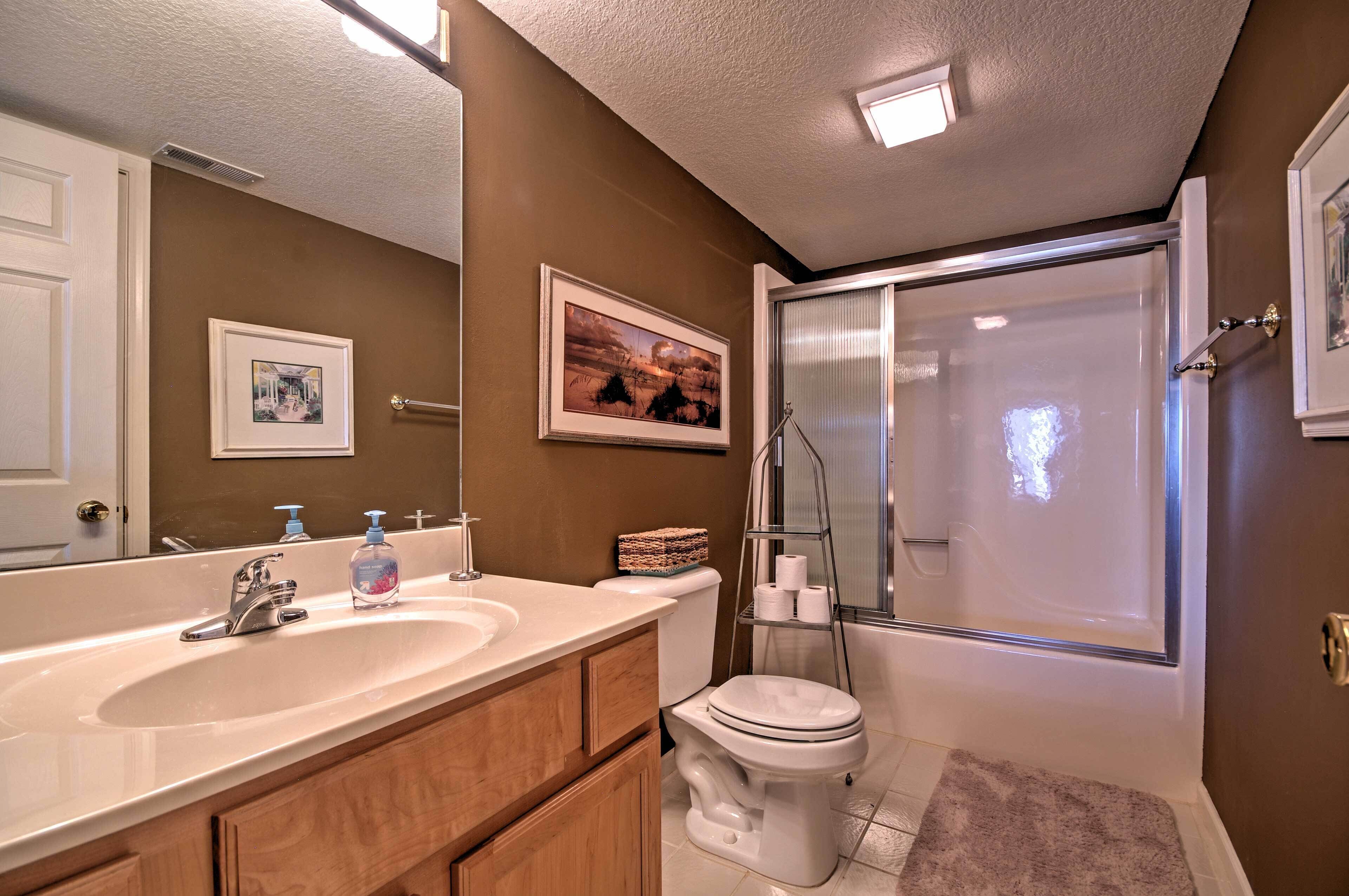 Une salle de bain avec un lavabo blanc, des toilettes et une douche. Des tableaux encadrés ornent le mur, et il y a un porte-serviettes.
