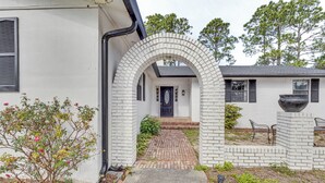 Une maison avec un portail en briques menant à la porte d’entrée, un petit jardin avec un chemin et un grand bac à fleurs.