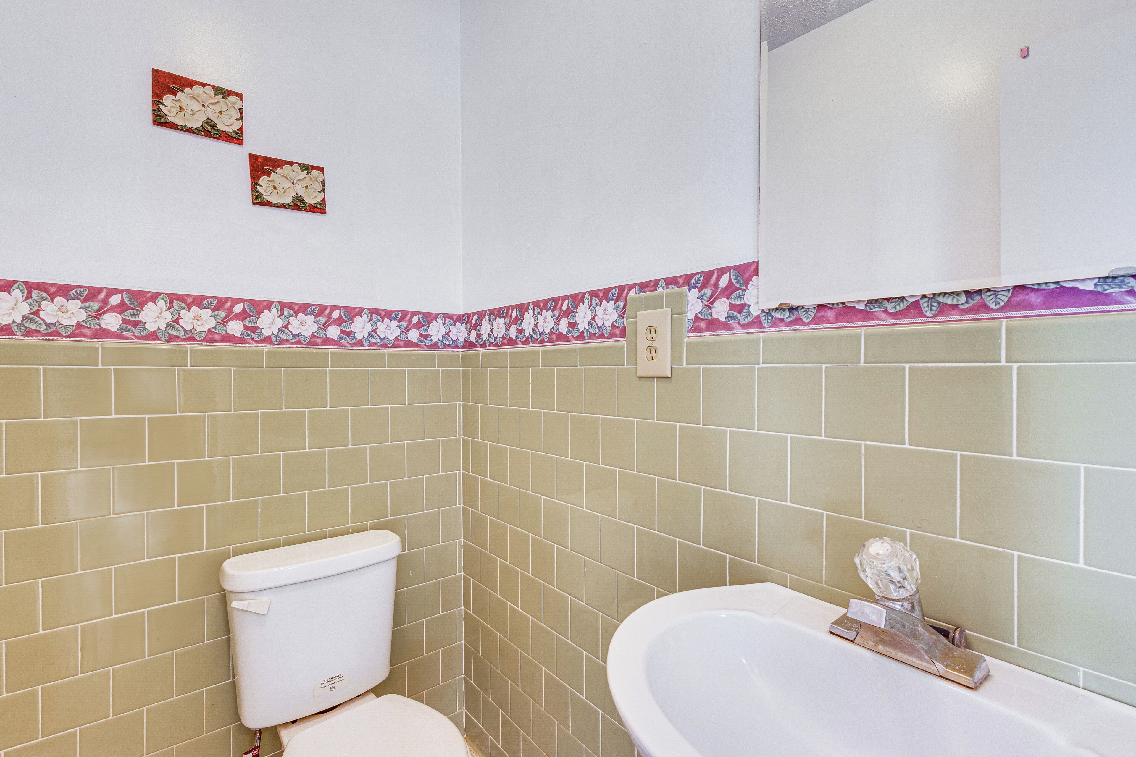 A bathroom with beige tiles, a white toilet, and a white sink with a glass object on it.