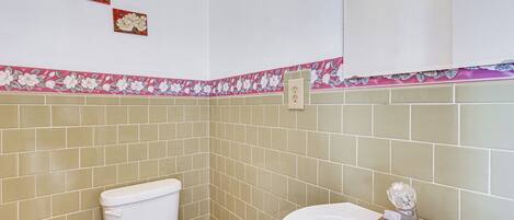 Un bany amb rajoles beix, un vàter blanc i un lavabo blanc amb un objecte de vidre a sobre.