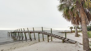 Une jetée en bois s’étendant dans une eau calme, entourée d’une plage de sable et de palmiers.