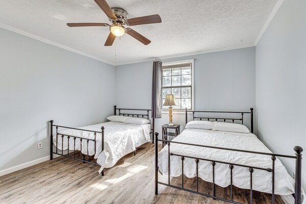 A bedroom with two single beds, a ceiling fan, a window with curtains, and a lamp on a nightstand. - Steps to Beach: Carrabelle Family Home w/ Patio! (Carrabelle)