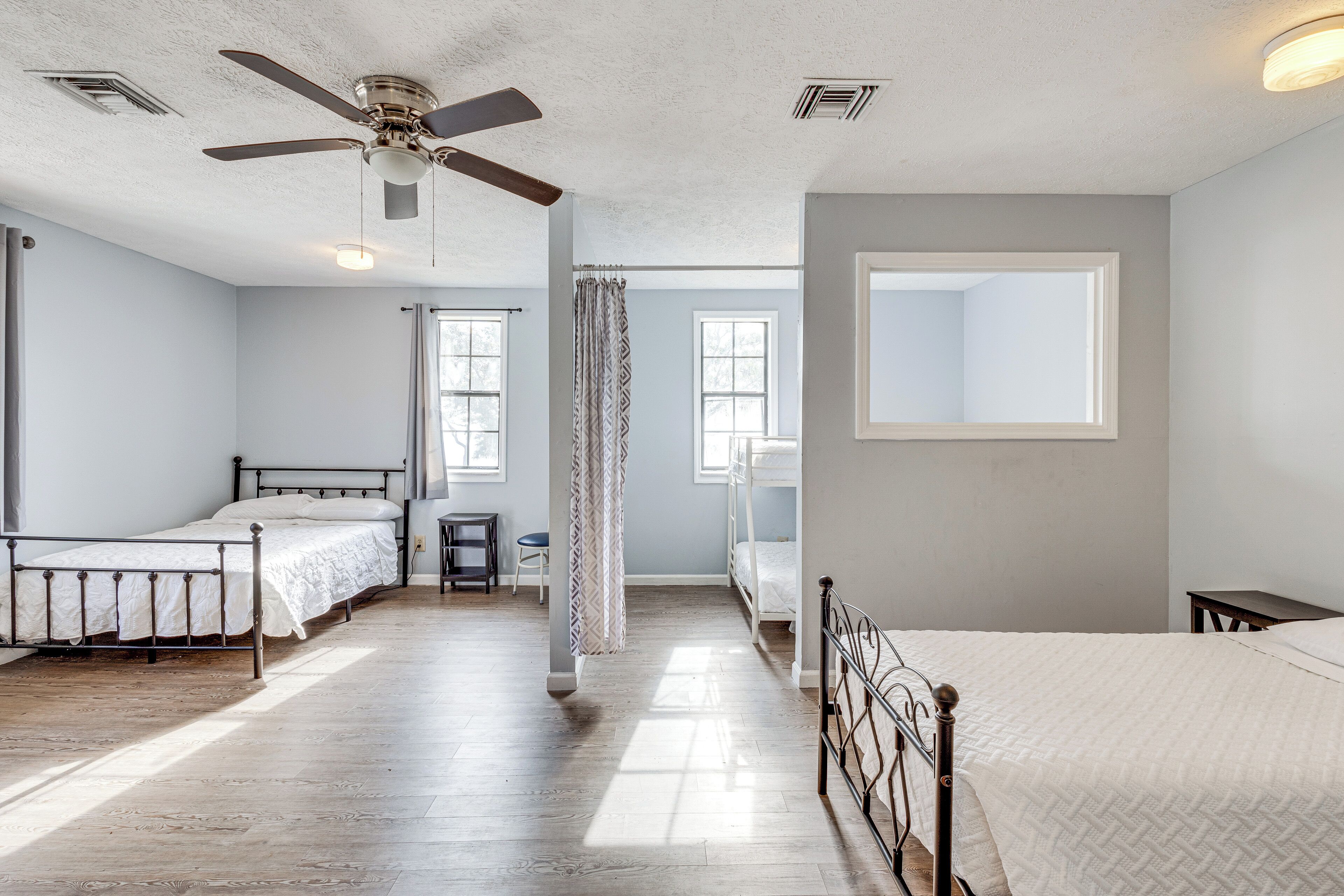 A room with three single beds, a ceiling fan, and a large window providing natural light.