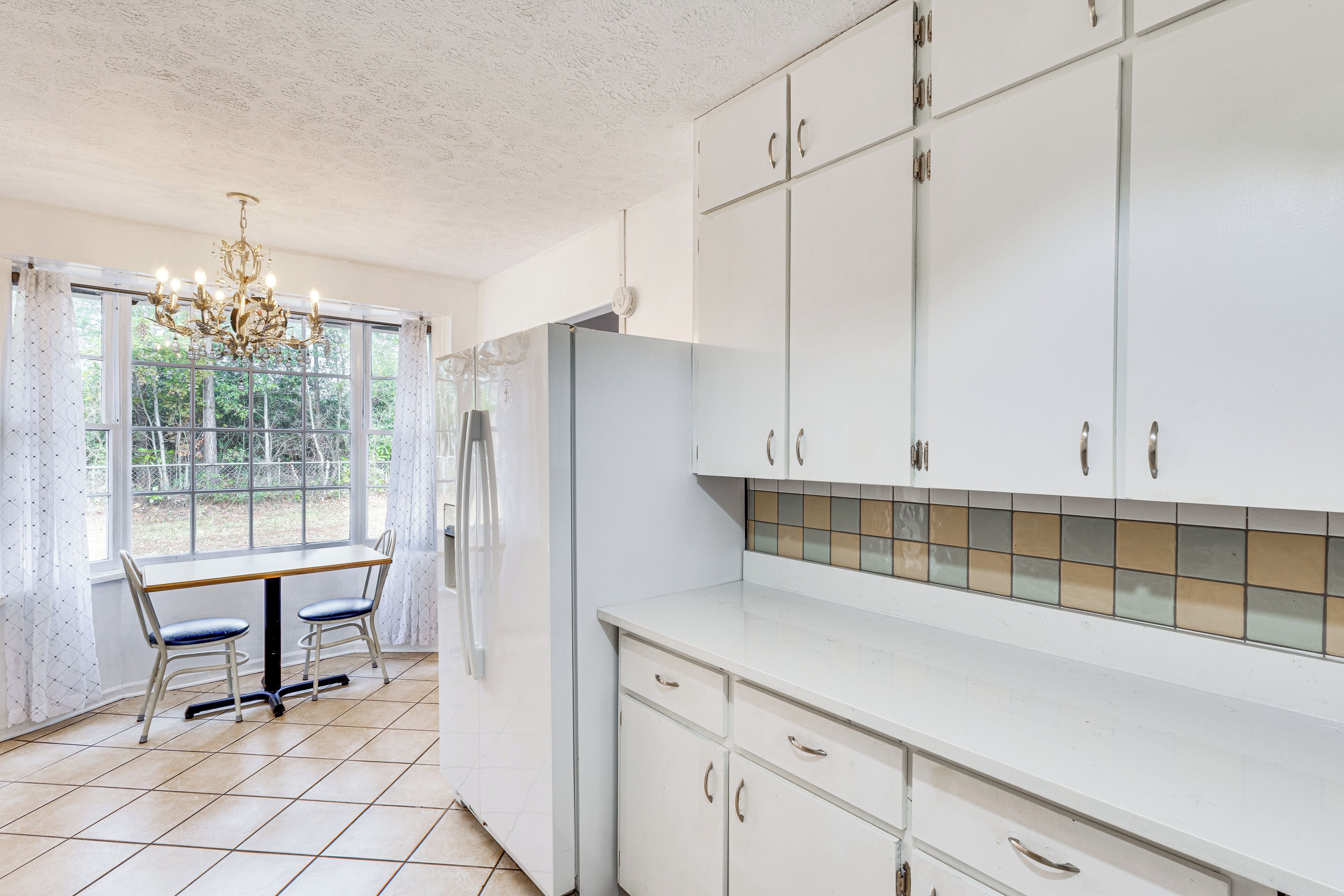 A kitchen with white cabinets, a tiled backsplash, and a dining table with chairs.