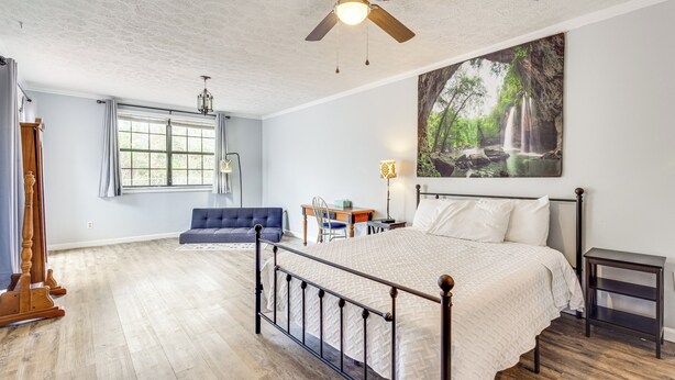 Une chambre avec un grand lit, un ventilateur de plafond, une fenêtre avec des rideaux, un bureau et une chaise.