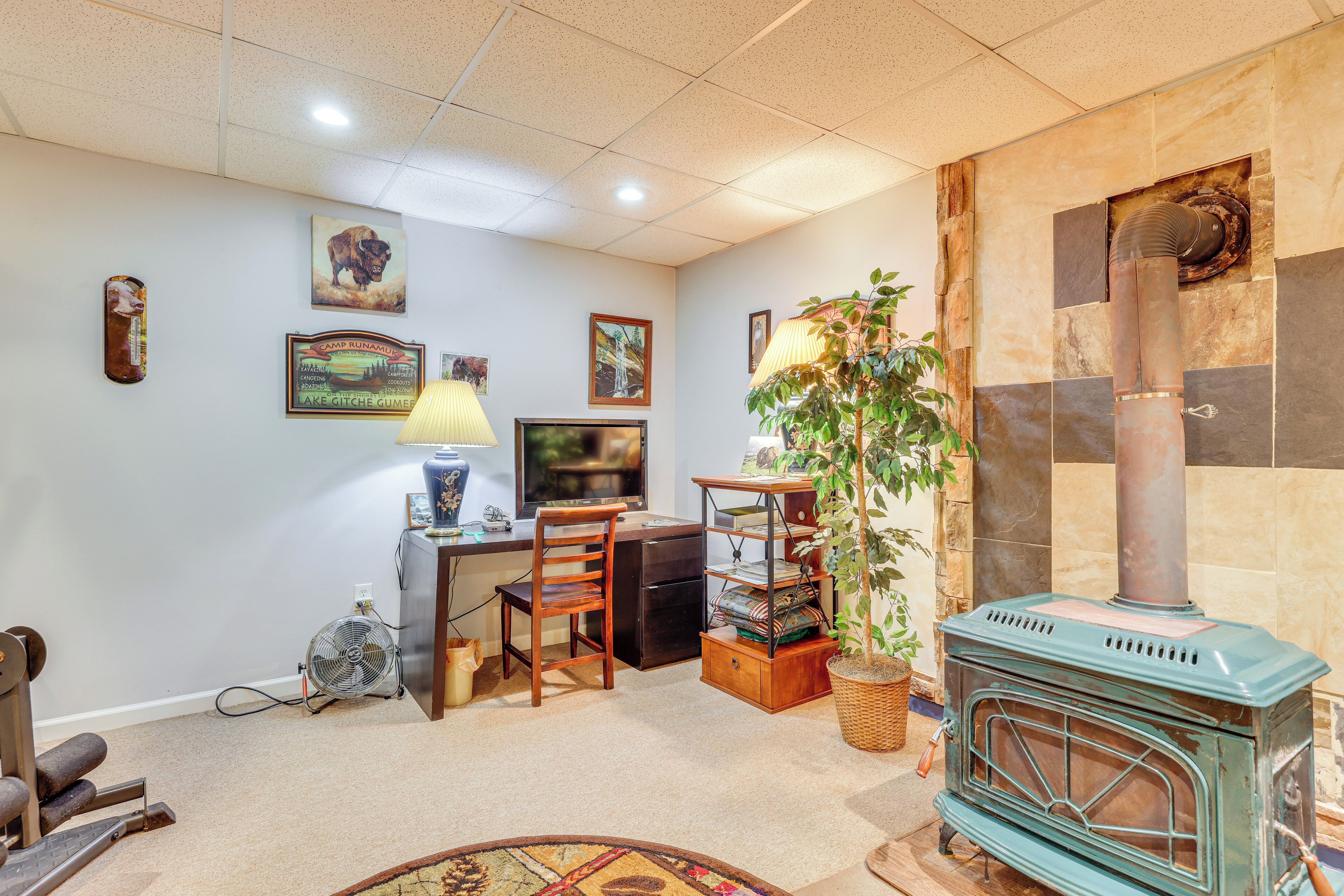 A cozy living room with a vintage stove, a desk with a computer, a chair, and a fan.