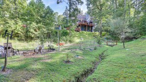A house with a deck, surrounded by a grassy area with trees and a small stream. - Georgia Home w/ 2 Fire Pits & Creek Access! (Young Harris)