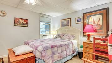 A bedroom with a bed, dresser, and a chair. There is a window with blinds, a ceiling fan, and a clock on the wall.