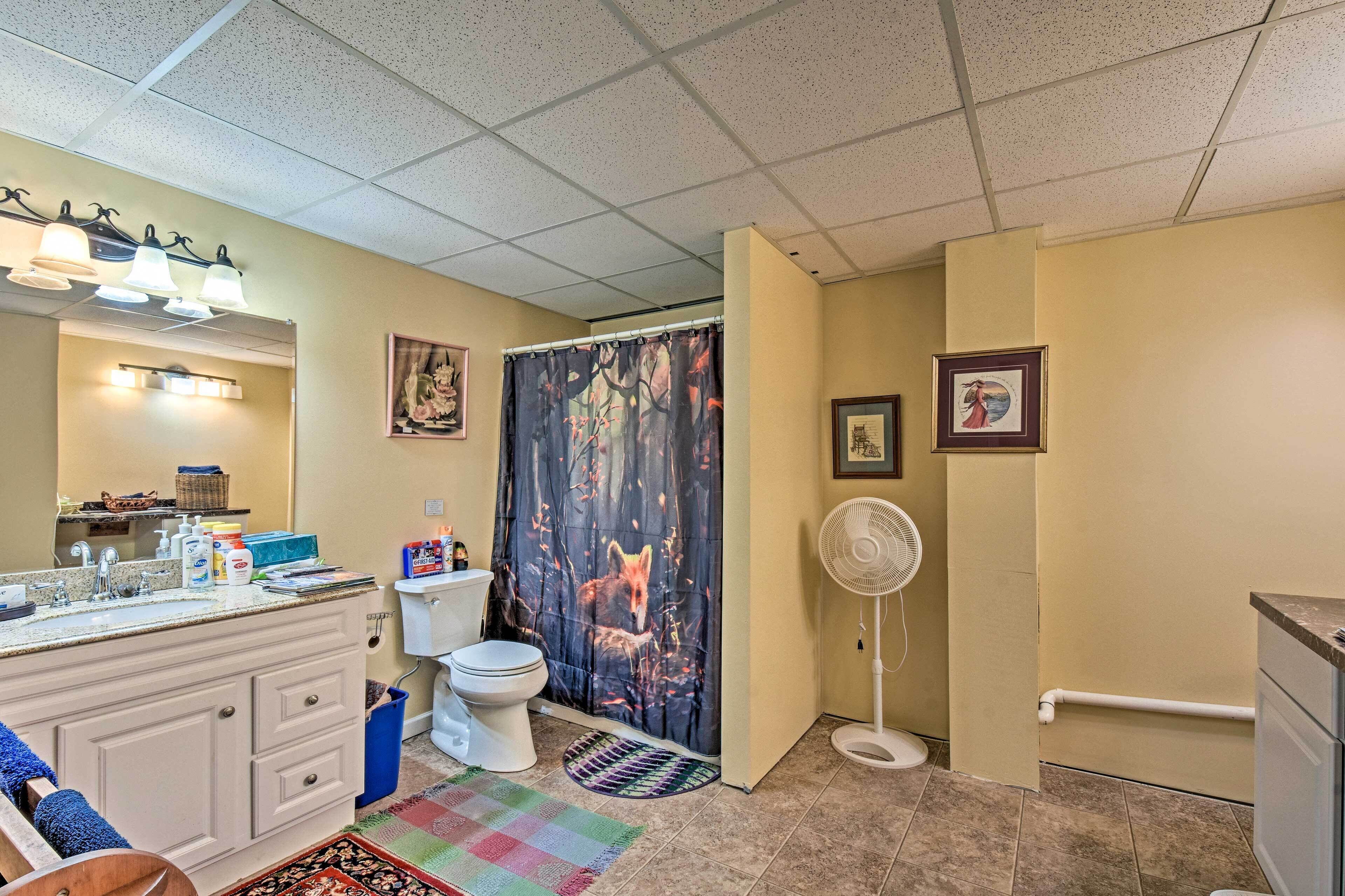 Une salle de bain équipée de toilettes, d’un lavabo et d’un rideau de douche orné de motifs de renard. On y trouve également un ventilateur et un petit tapis sur le sol.