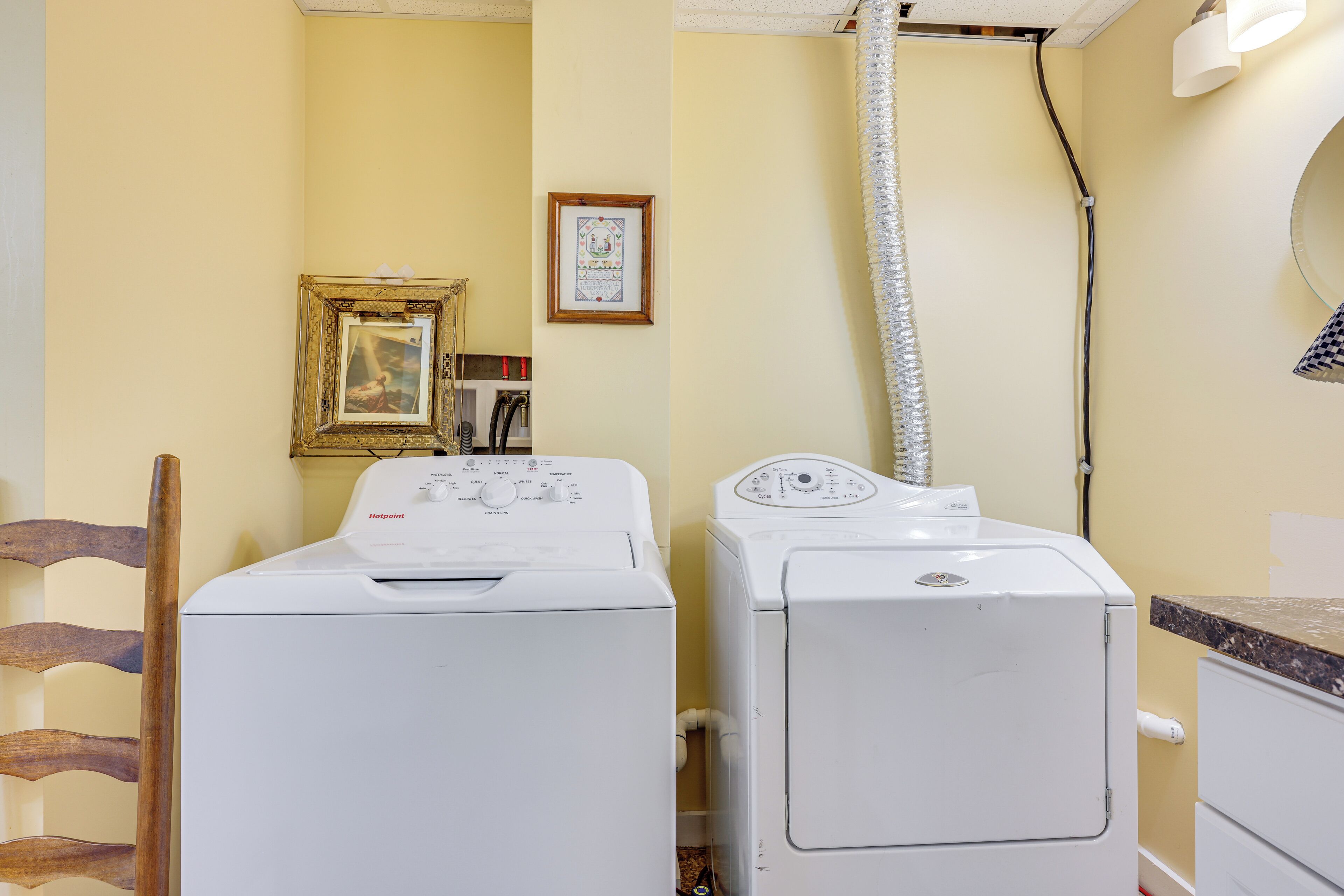 A laundry area with two washing machines, a wooden chair, a framed picture, and a mirror on the wall.