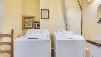 A laundry area with two washing machines, a wooden chair, a framed picture, and a mirror on the wall.