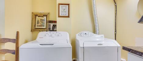 A laundry area with two washing machines, a wooden chair, a framed picture, and a mirror on the wall.