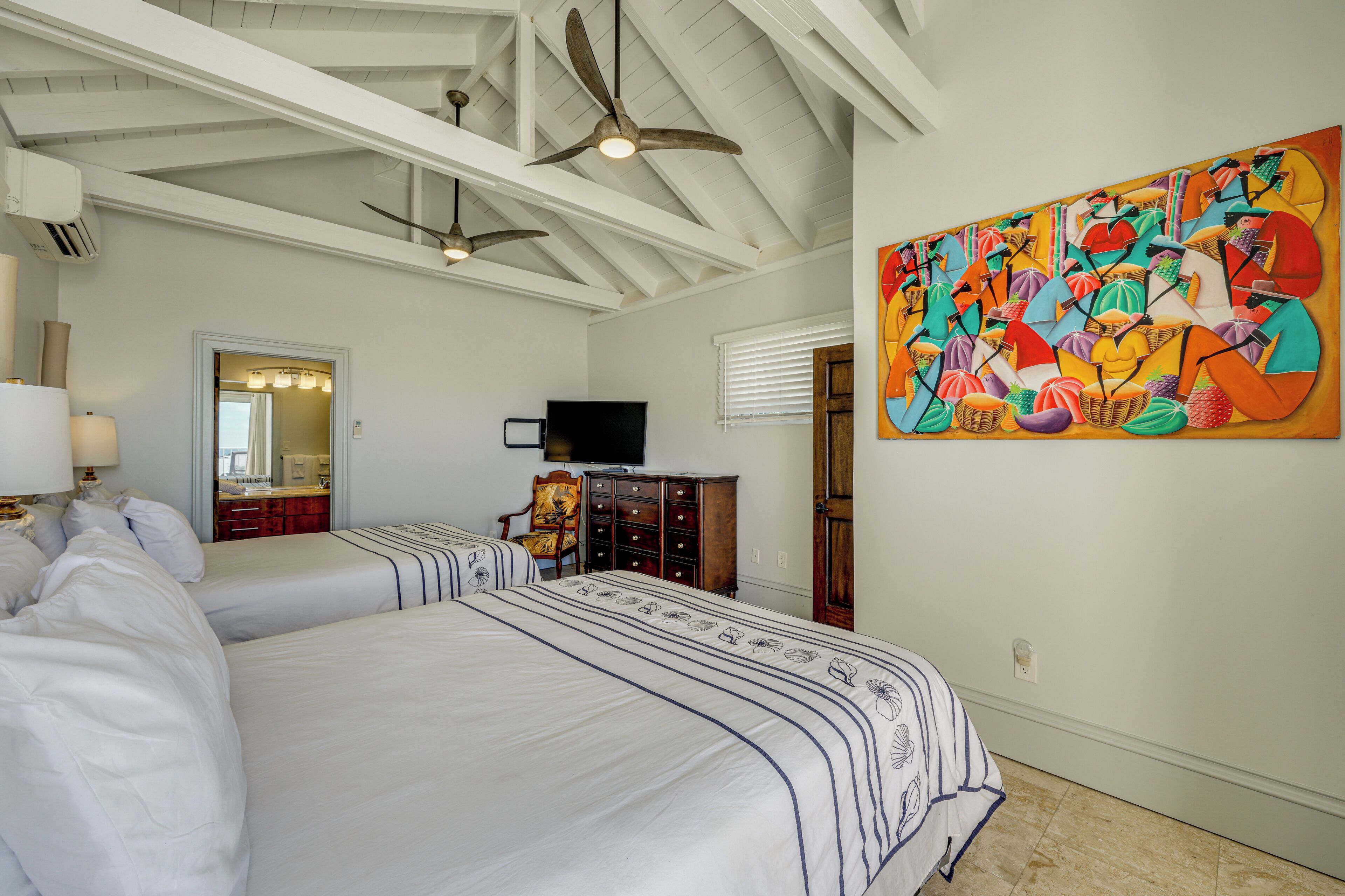 A hotel room with two beds, a ceiling fan, a large abstract painting, a television, and a wooden dresser.