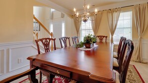 Een formele eetzaal met een grote houten tafel, zes stoelen, een kroonluchter en een potplant op de tafel.
