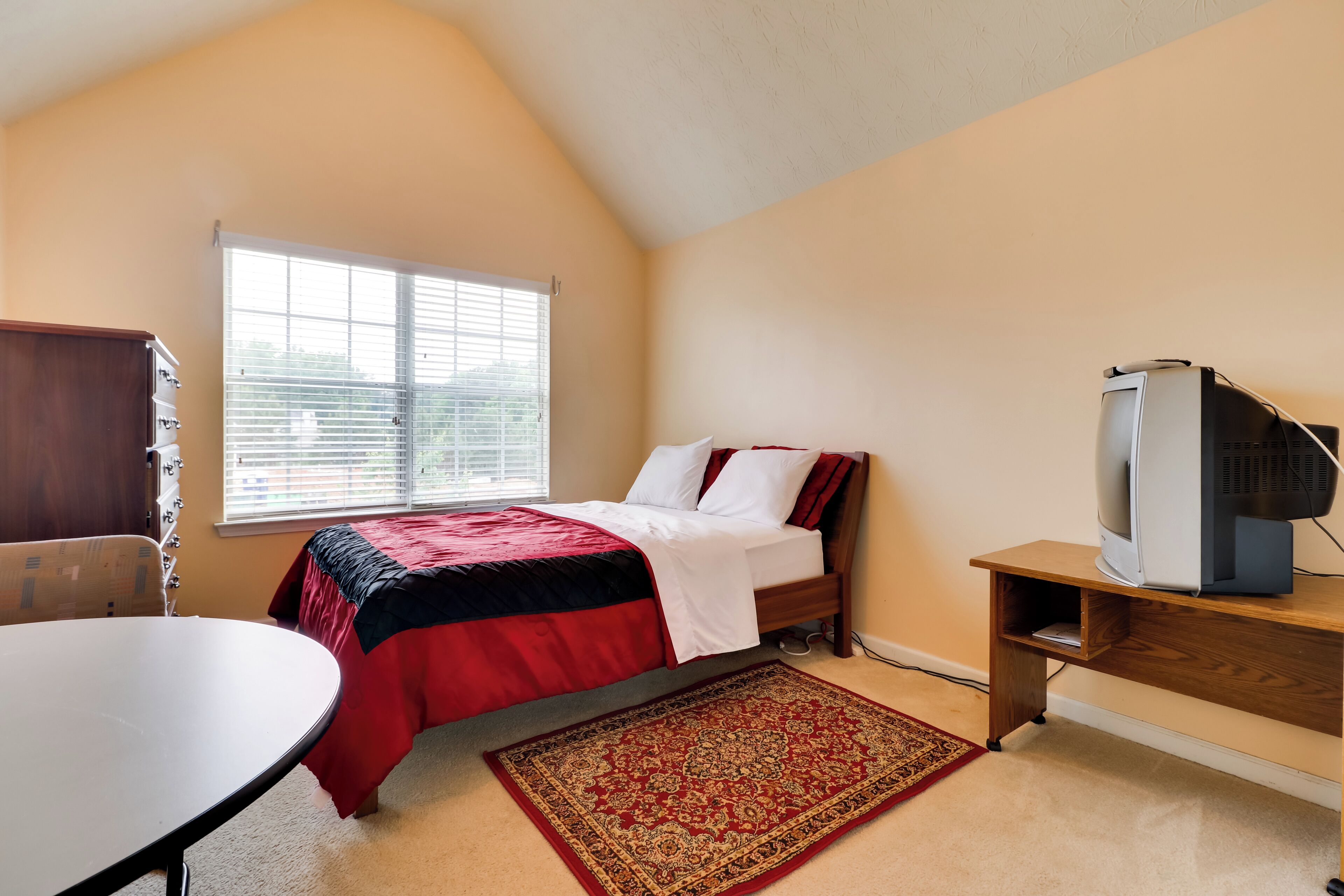 Ein Schlafzimmer mit Bett, Fernseher, Schreibtisch und Stuhl.
