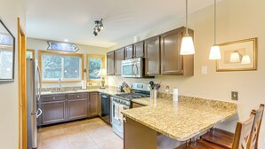 Cocina con encimeras de granito, electrodomésticos de acero inoxidable, armarios de madera e iluminación colgante.