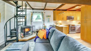 Una sala de estar acogedora con un sofá gris, una chimenea y una cocina con armarios de madera y electrodomésticos.