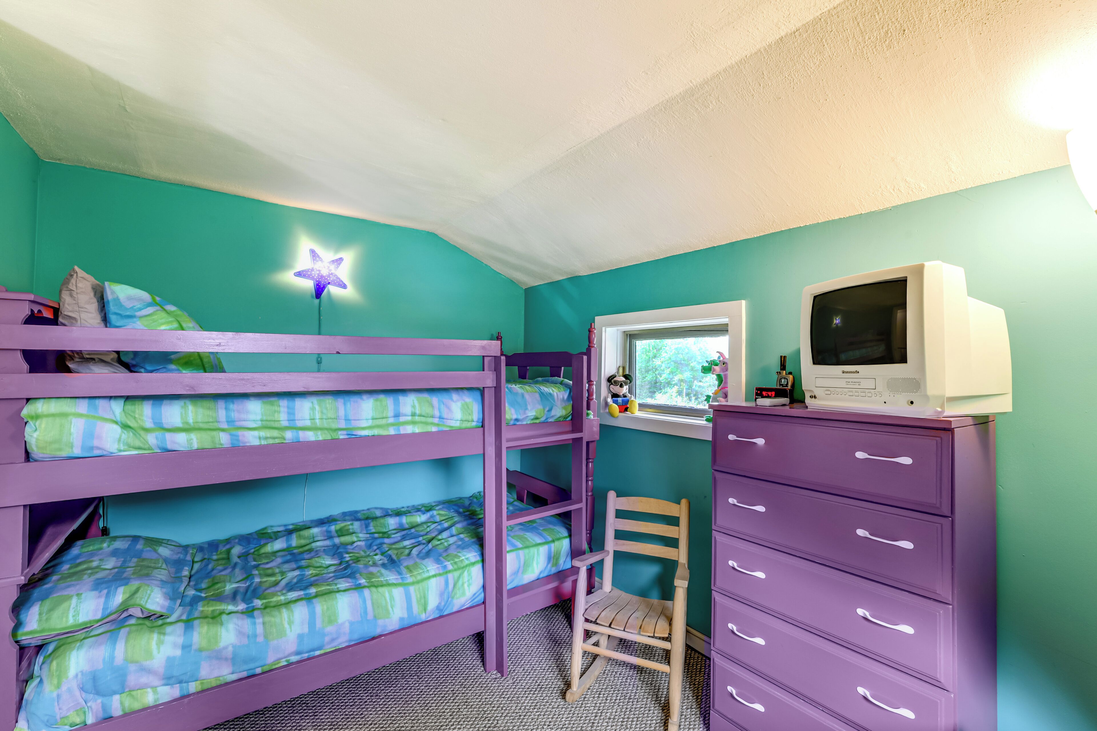A bunk bed room with a star-shaped ceiling light, a desk with a computer, and a purple dresser.