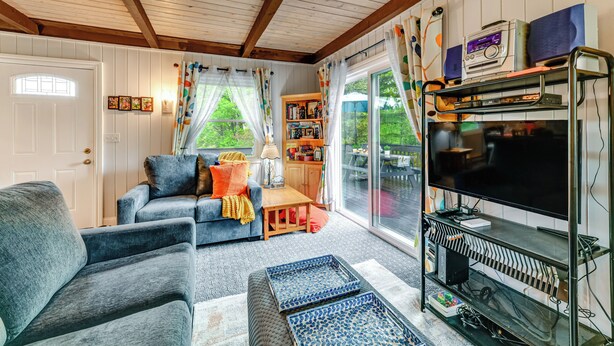 Una sala acogedora con un sofá, un sillón, un reposapiés, un televisor y una estantería.