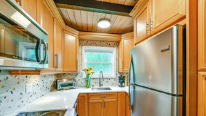 Una cocina con armarios de madera, un refrigerador de acero inoxidable, un microondas y una ventana con vista a la vegetación.