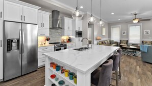 A modern kitchen with white cabinetry, stainless steel appliances, and a marble island. - Sea Breeze Cottage - Private Home At The Shores 3 Bedroom Home (South Padre Island)